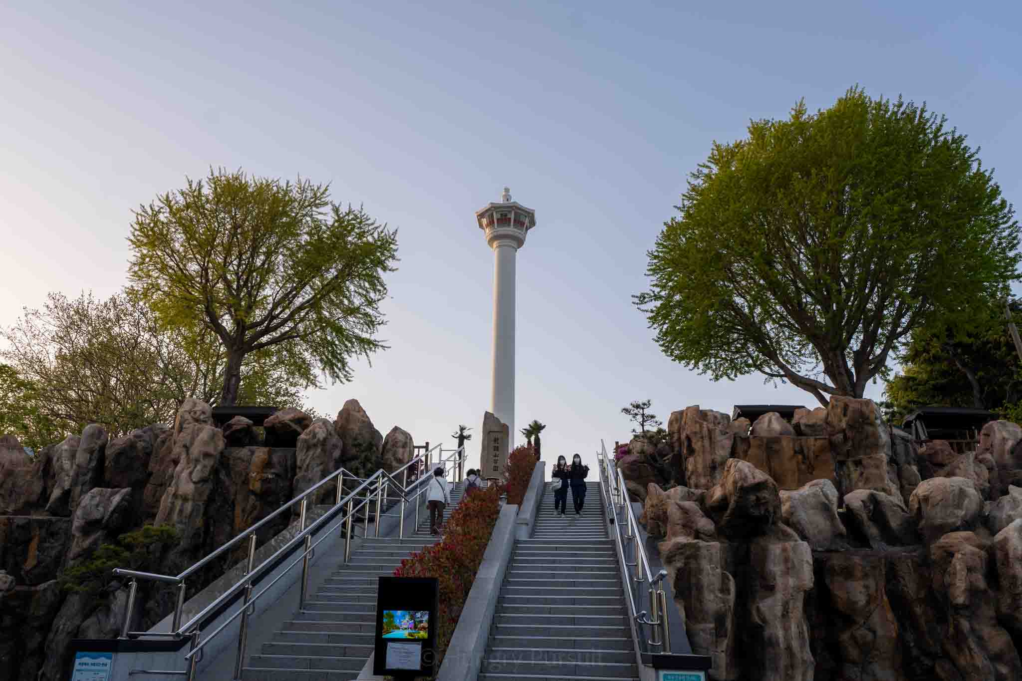 View of the Busan Tower from the base of the stairs with tourists taking photos