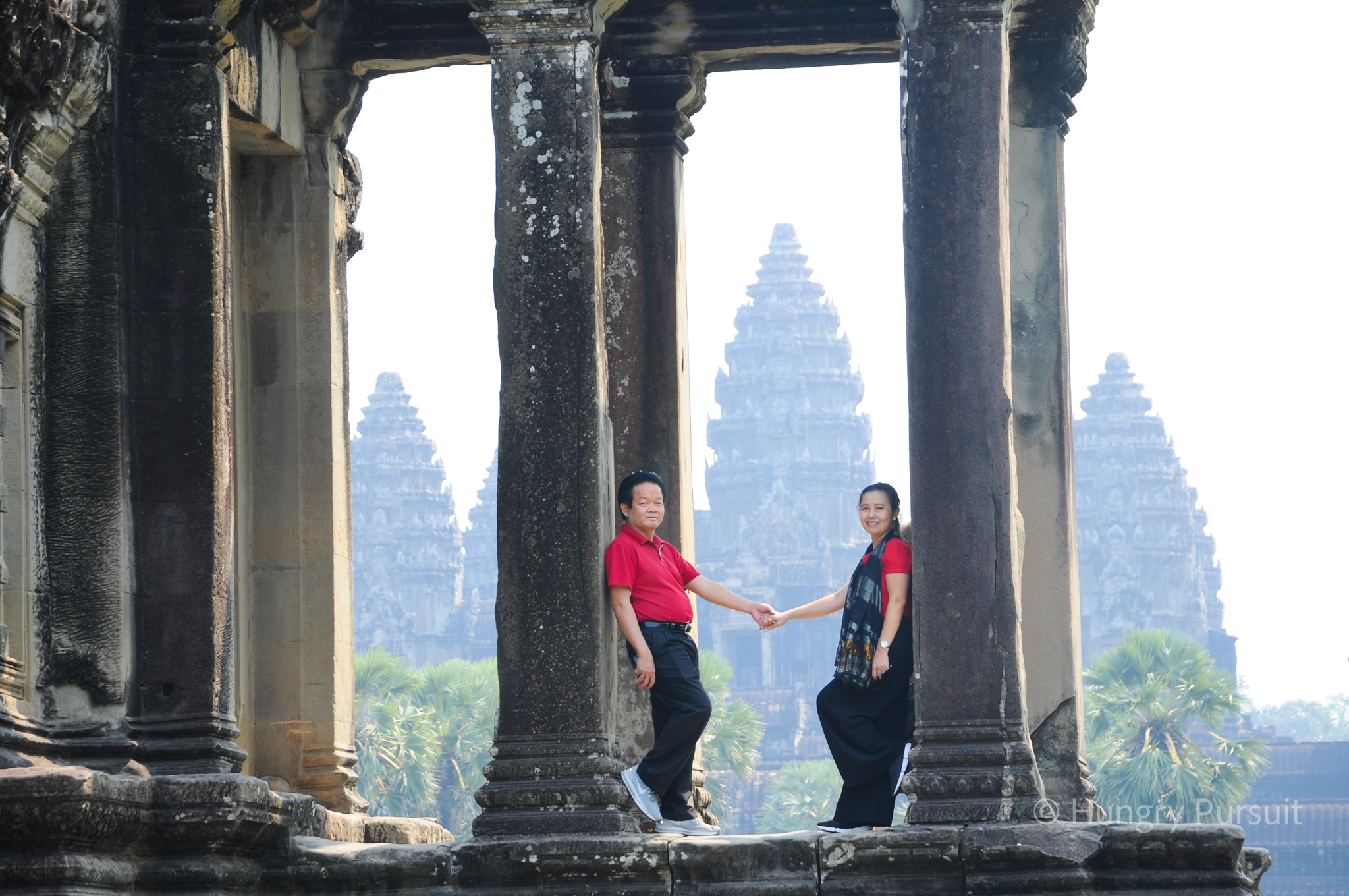 Mid-aged couple holding hands, standing in front of the majestic Angkor Wat temple in Cambodia.