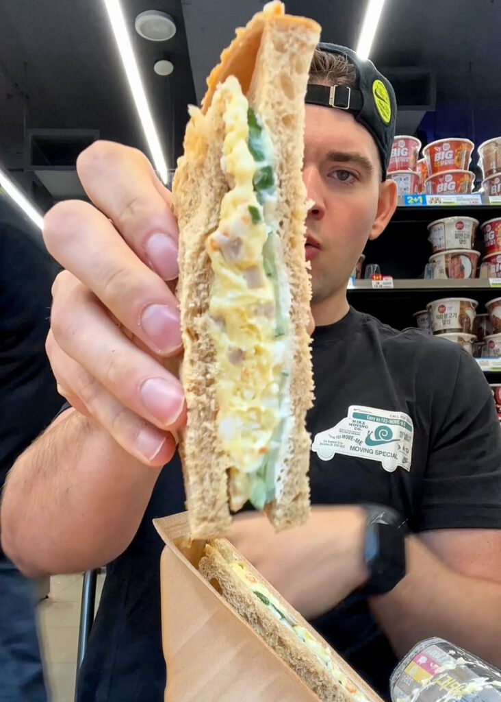 a man holding a korean egg sandwhich at a korean convenience store.