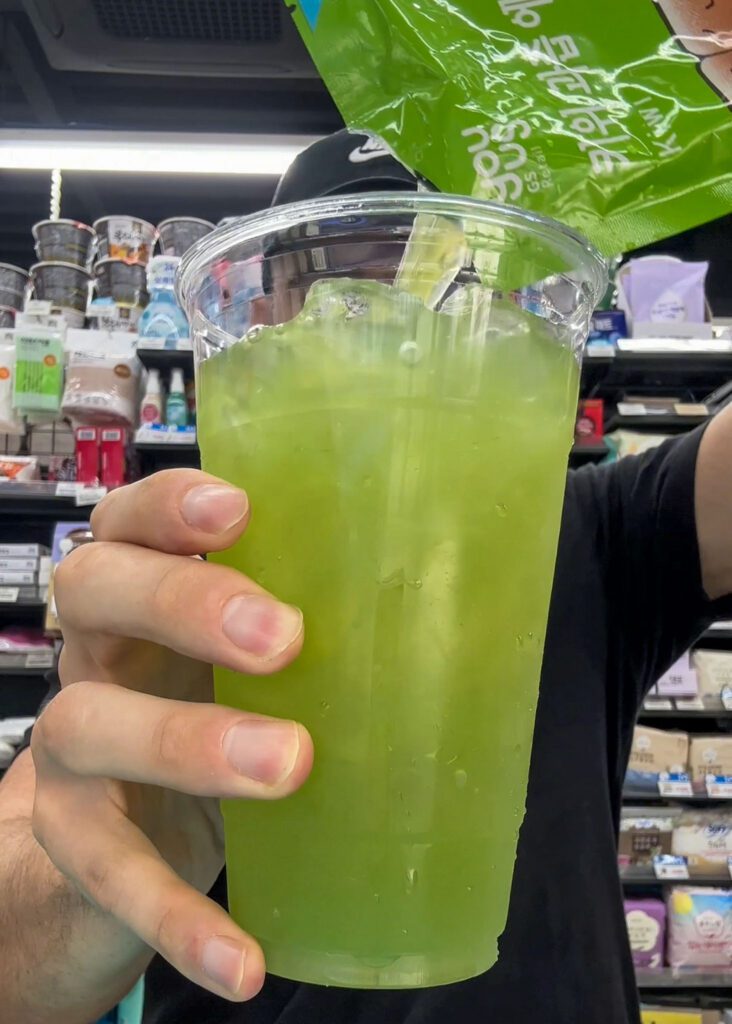 a man holding korean drink pouches pouring it into a korean ice cup at a korean convenience store.