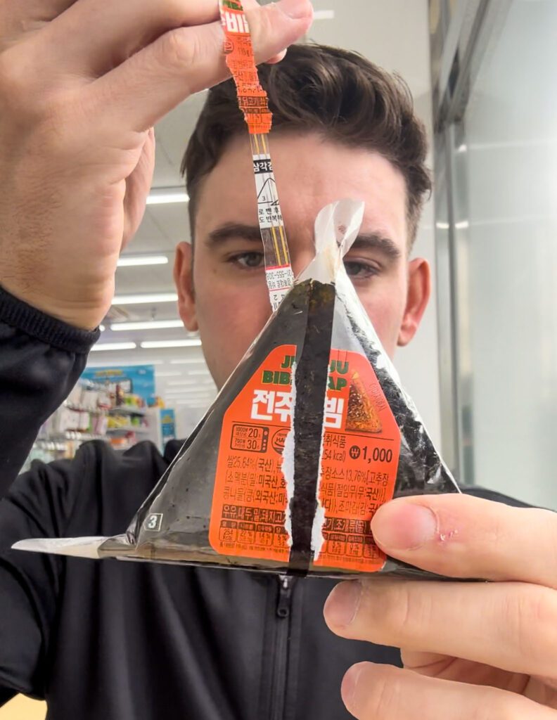 a man opening a onigiri at a korean convenience store.