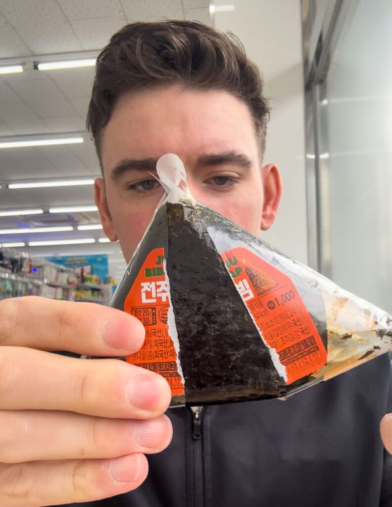 a man in the process of opening a onigiri at a korean convenience store.