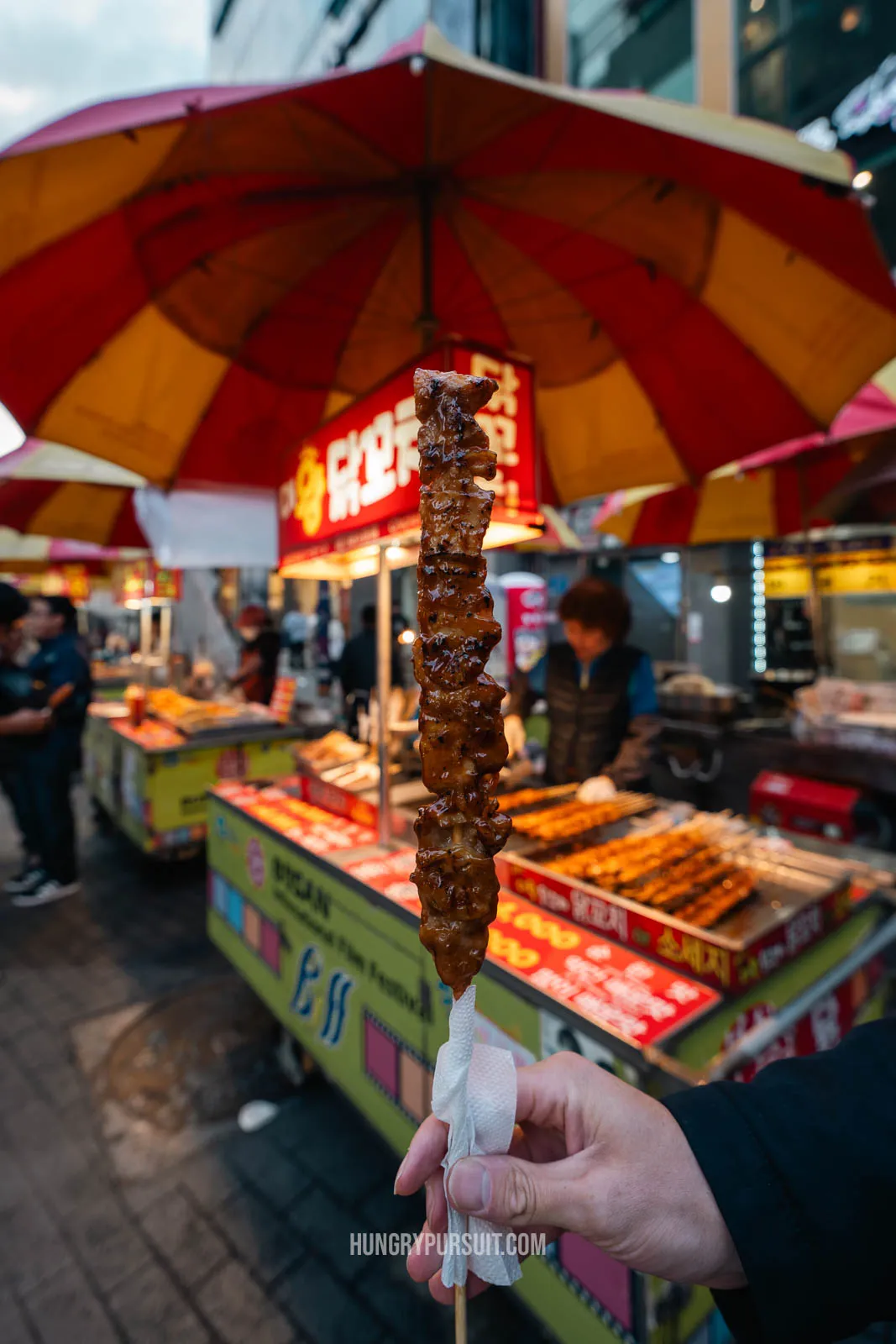 a man holding street food chicken skewer at Biff Square; things to do in busan