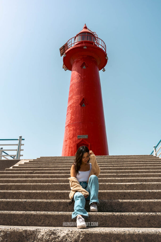 a woman looking down posing in front of the red lighthouse at haeundae blueline park photos