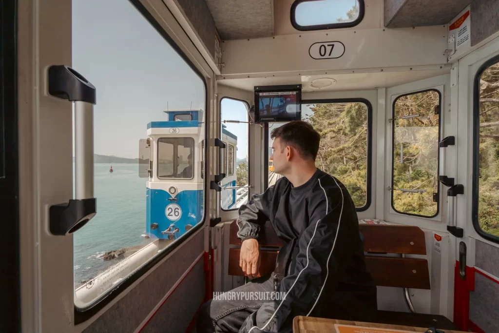 a man looking outside the window of a Haeundae sky capsule in Haeundae blueline park.