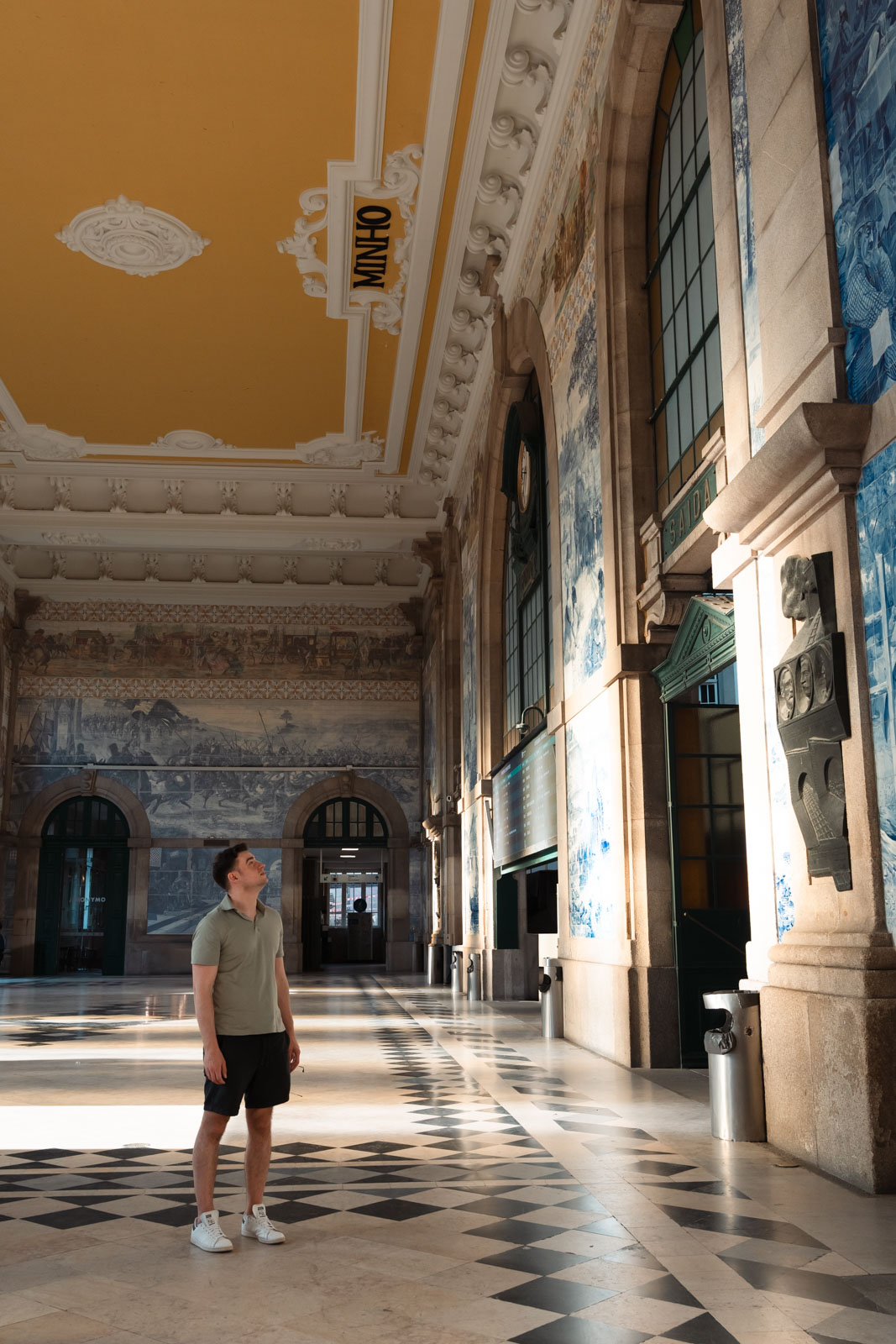 a man standing observing the blue and white tiles inside Sao Bento Train Station; 2 days in porto itinerary.