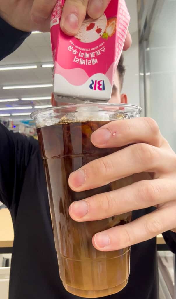 a man squeezing korean milk into his coffee Korean drink pouches at a korean convenience store.