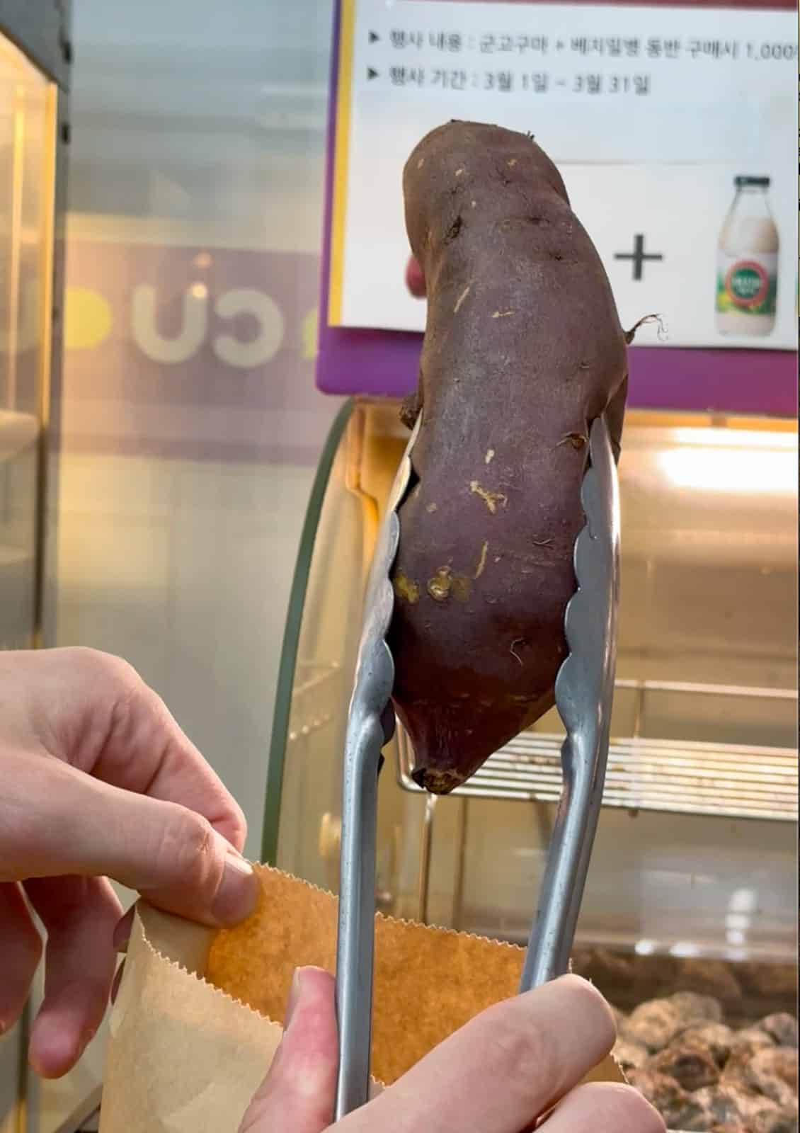 a man holding a korean sweet potato with tongs in a korean convenience store.