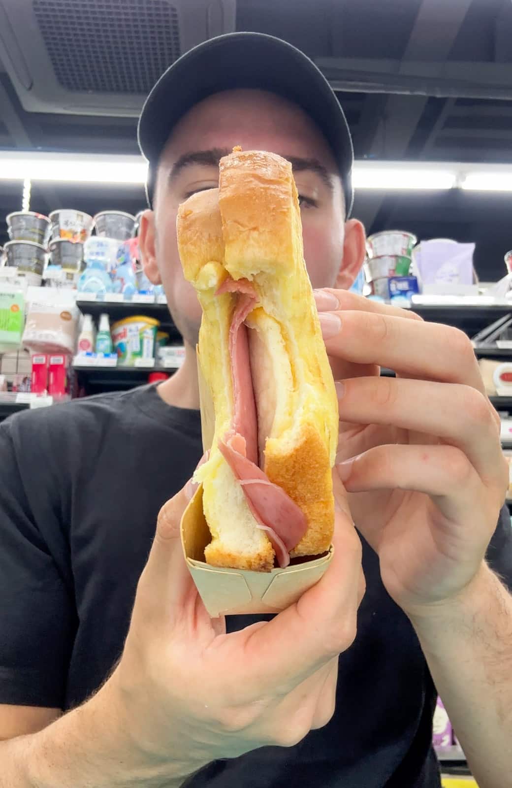 a man showing the inside of the korean toast with egg & ham at a korean convenience store.